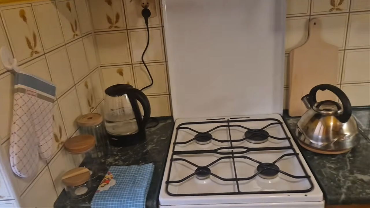Wolnostojąca kuchenka gazowa, po lewej stronie znajduje się czajnik elektryczny, a po prawej gazowy.