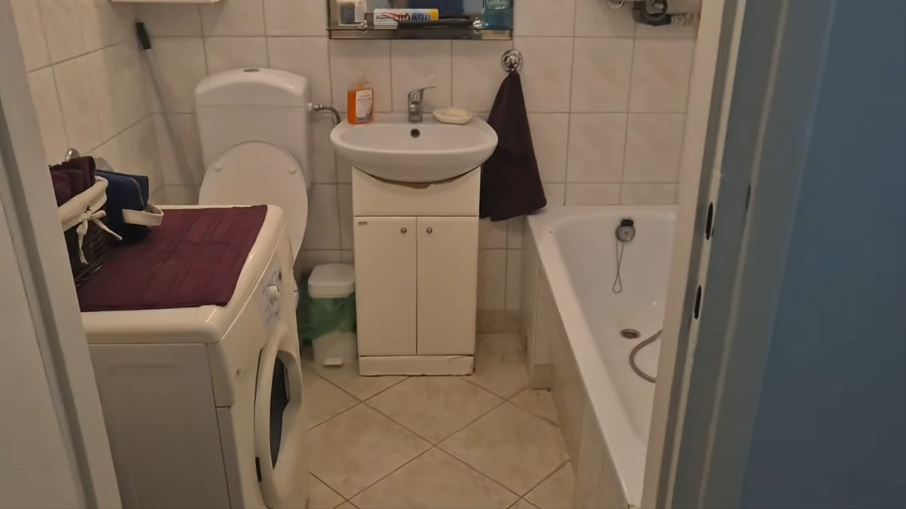 Widok na łazienkę w kawalerce. W kadrze umywalka, wanna, pralka