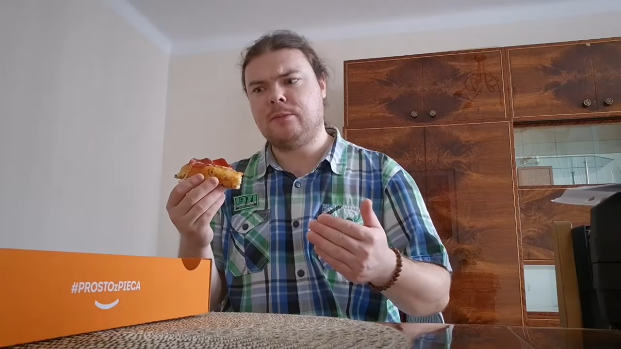 Kacper Bednarczyk siedzi przed pudełkiem pizzy i degustuje jej kawałek